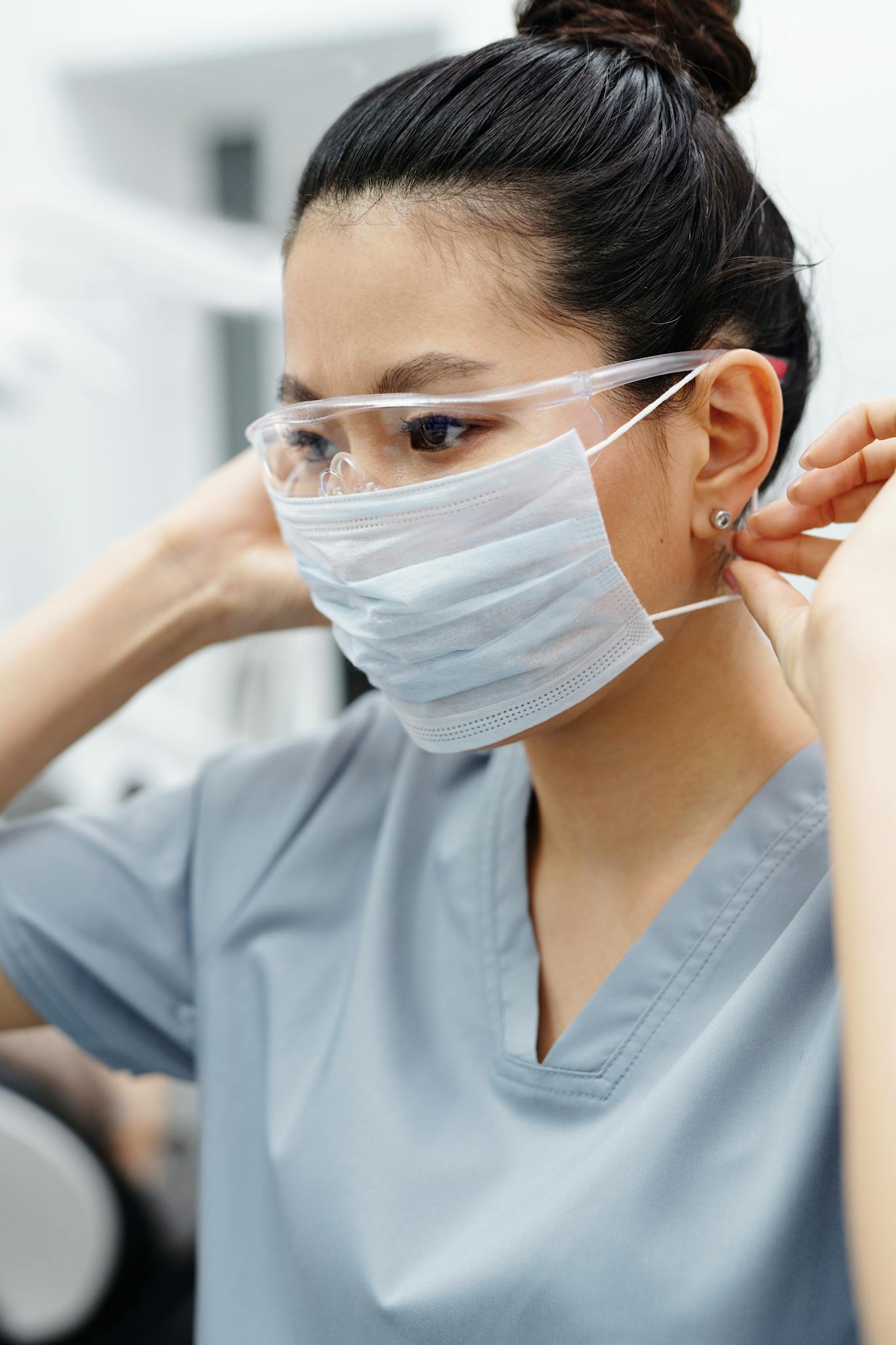 Asian woman healthcare professional adjusting face mask and goggles indoors.